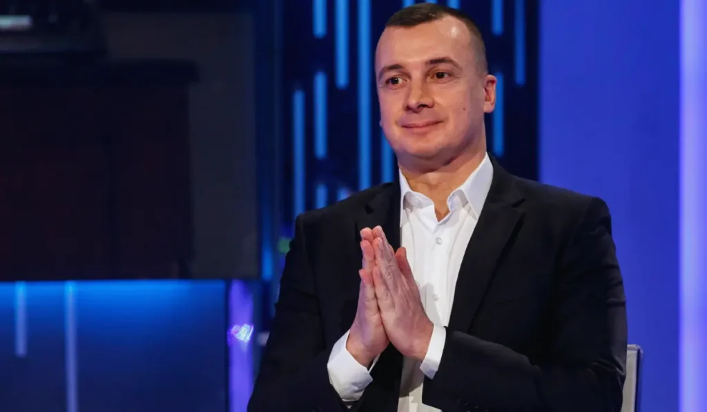 Rocco Casalino sorridente in un ritratto pubblico, sfondo neutro da intervista